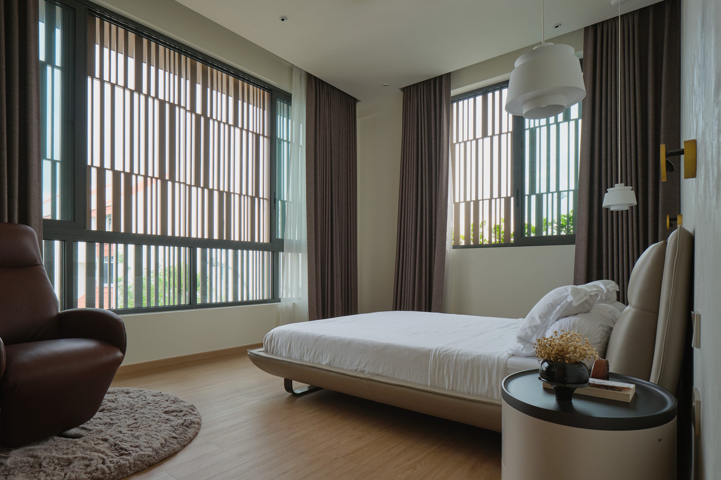 Bedroom with daylight filtered through the gridded screens, soft neutral furnishing and a leather bed