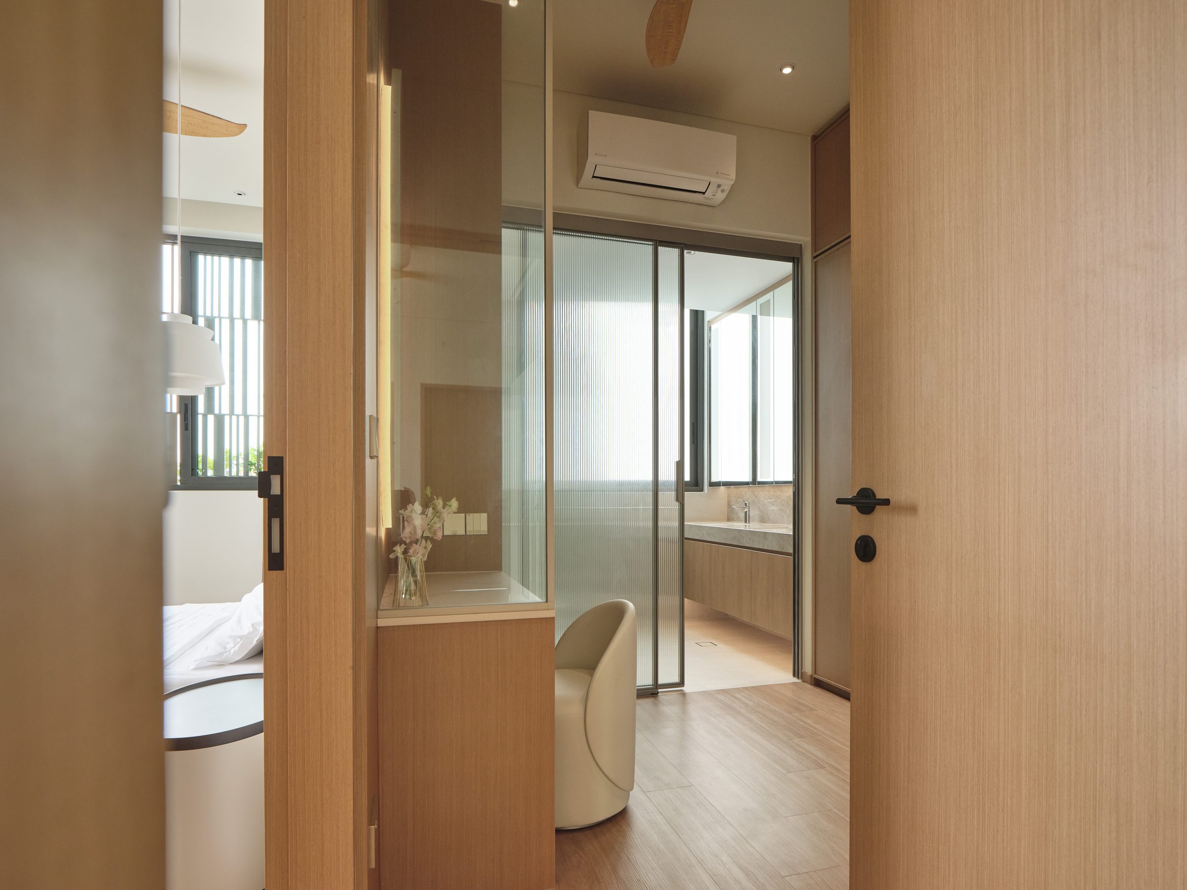 Threshold between bedroom and ensuite, with fluted glass screening the vanity beyond an oak door