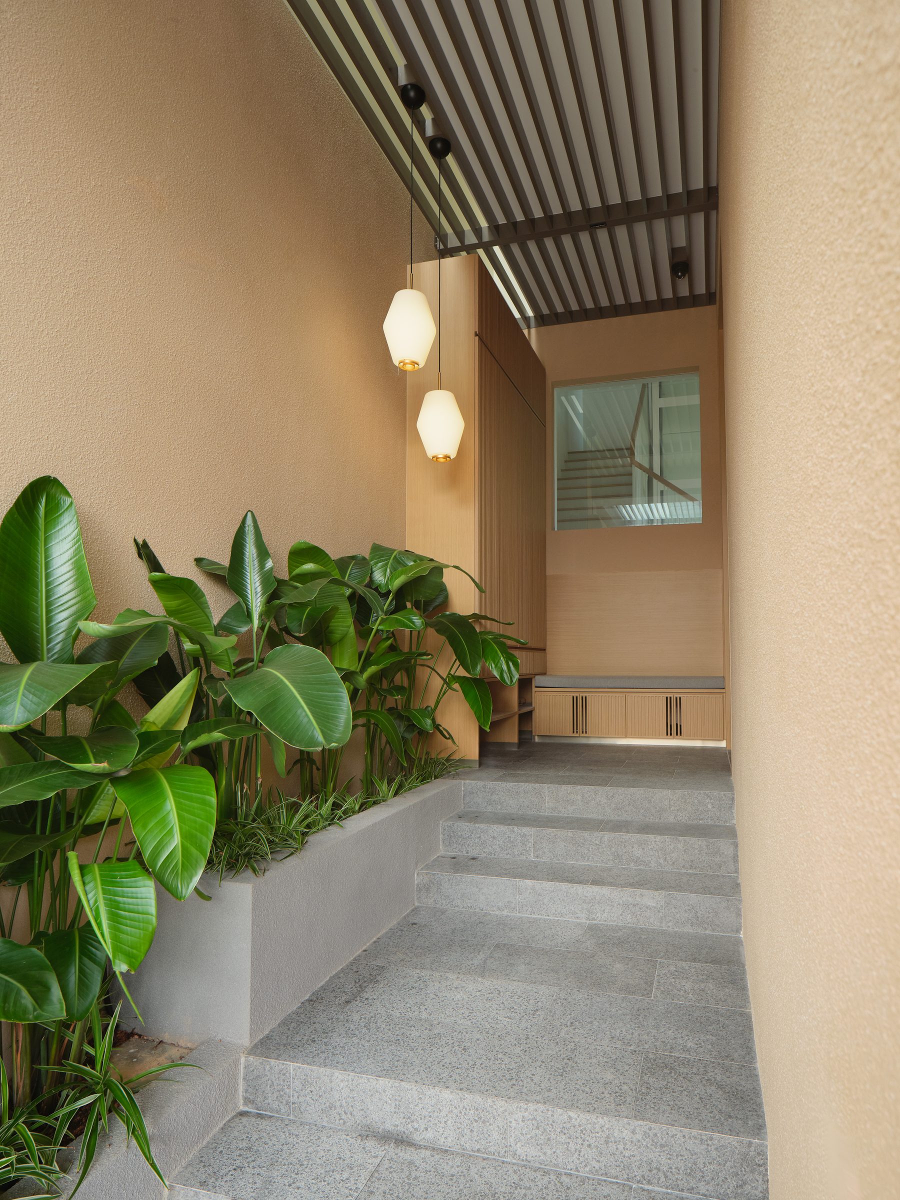 Planted entry stair flanked by a stone planter of heliconias, with two pendant lanterns hanging over the timber-lined threshold