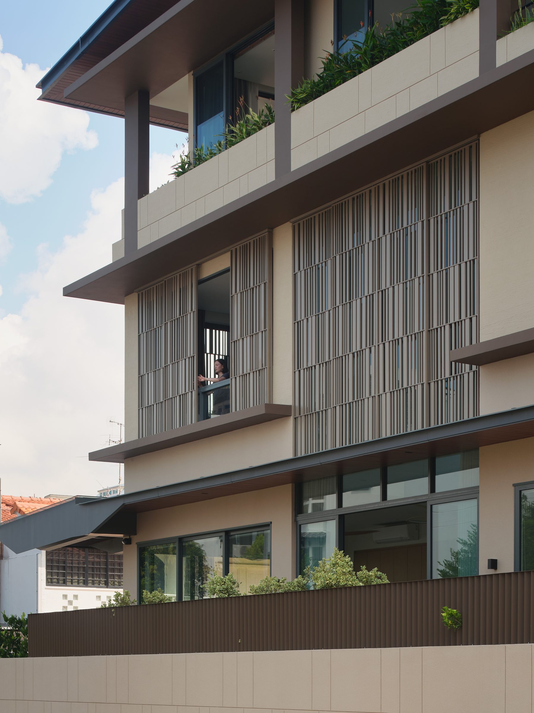 Looking up under the deep overhangs at layered timber screens, an open window and planted balcony edges
