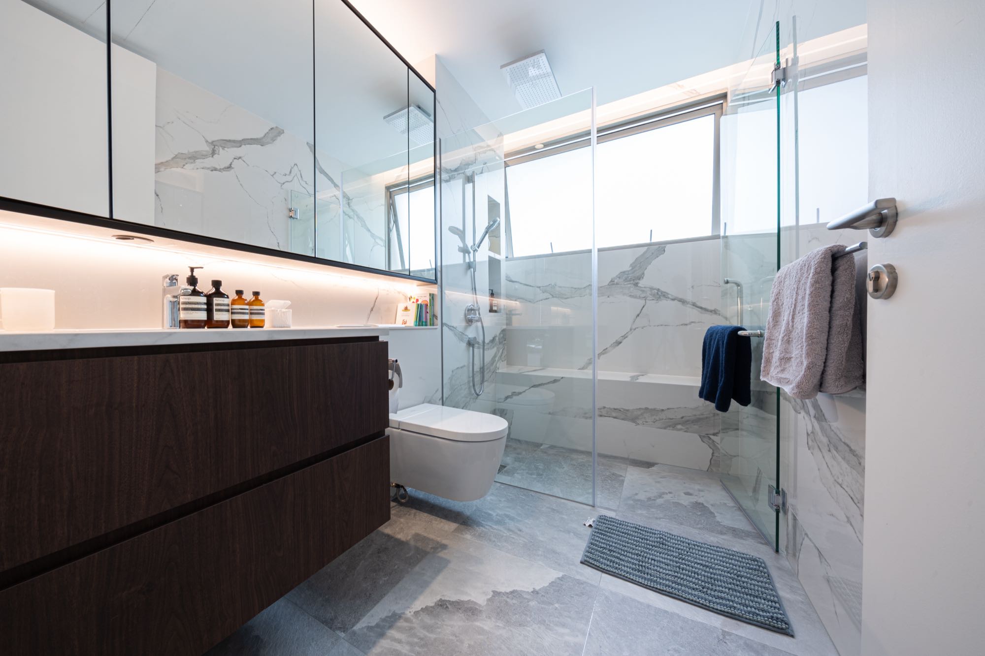 Master bathroom finished in bold-grain white marble with a dark walnut vanity and walk-in shower