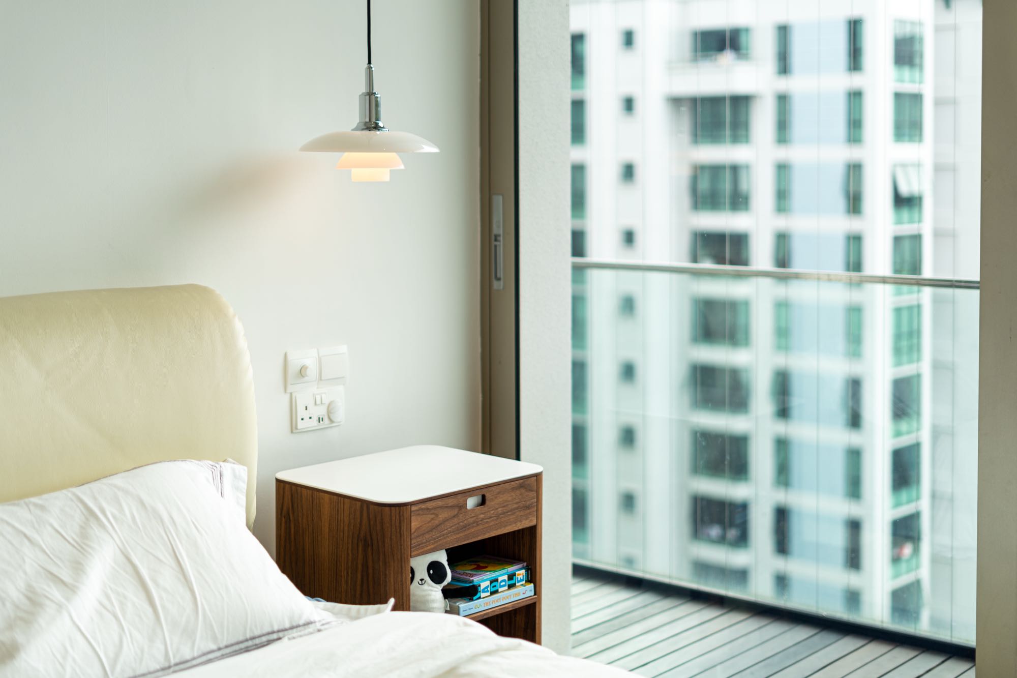 Master bedroom with cream upholstered headboard, balcony view, and Louis Poulsen pendant lighting