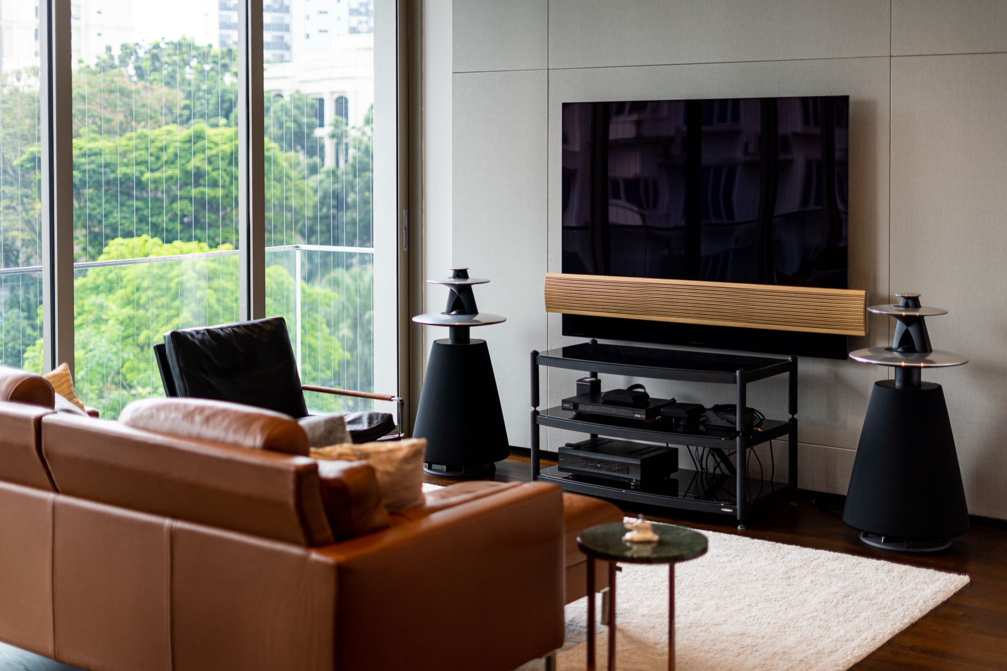 Living area with B&O speakers, acoustic-paneled wall behind the television, and view to greenery