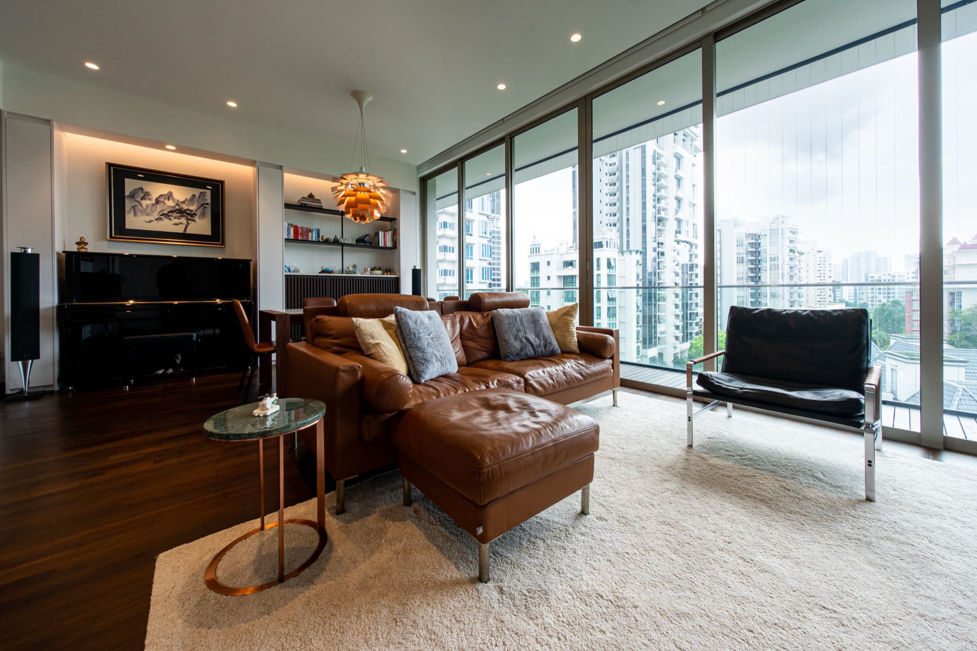 Wide view of the living room with leather sofa, B&O Beolab speakers, and floor-to-ceiling skyline view
