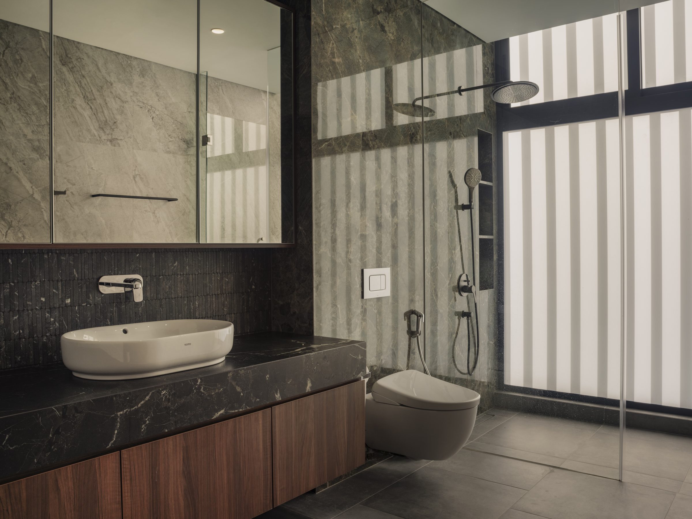 Bathroom in dark figured marble, wall-hung basin and a walk-in shower behind glass
