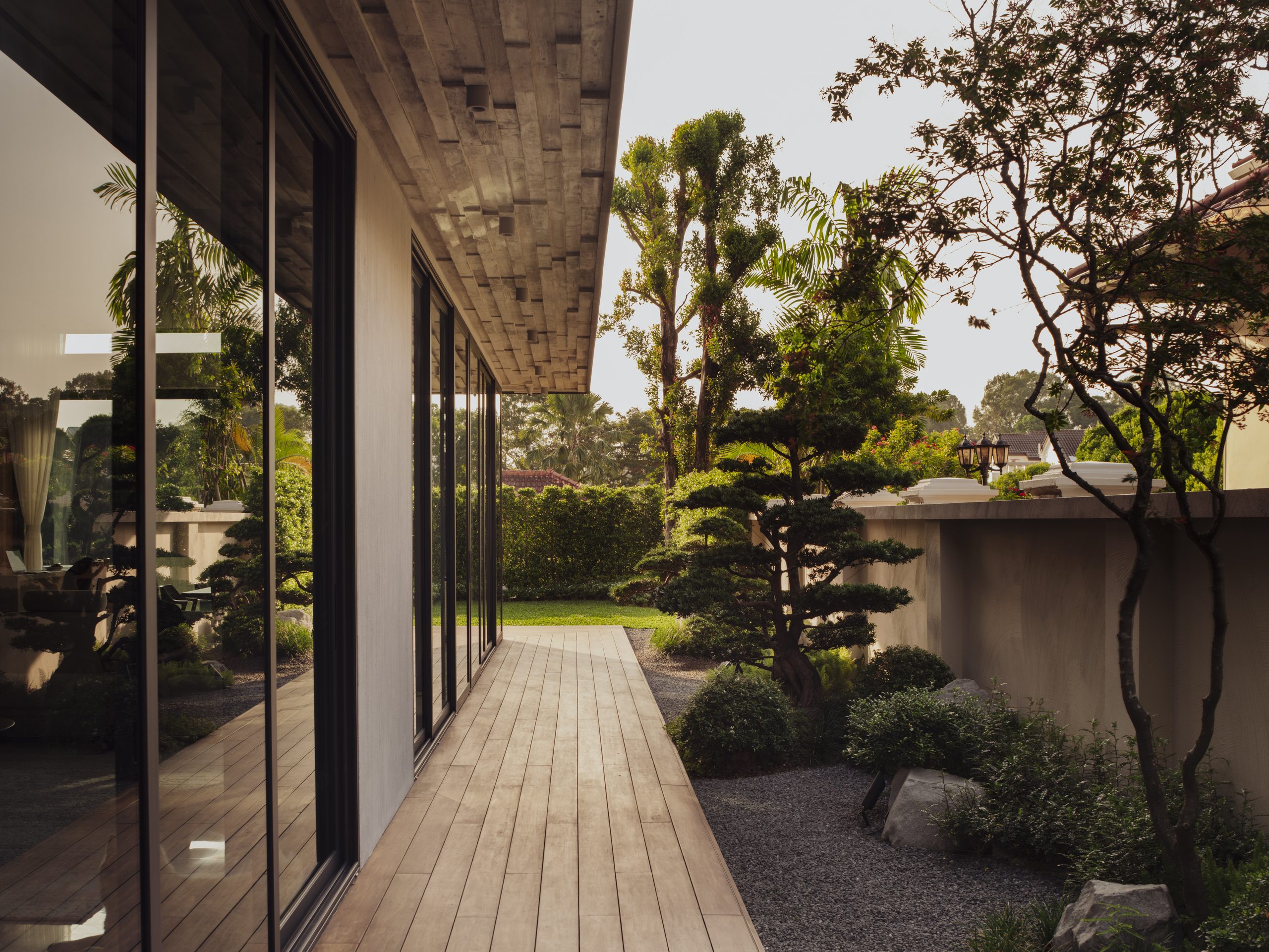 Timber deck running along the glazing, edged with gravel, bonsai and mature planting