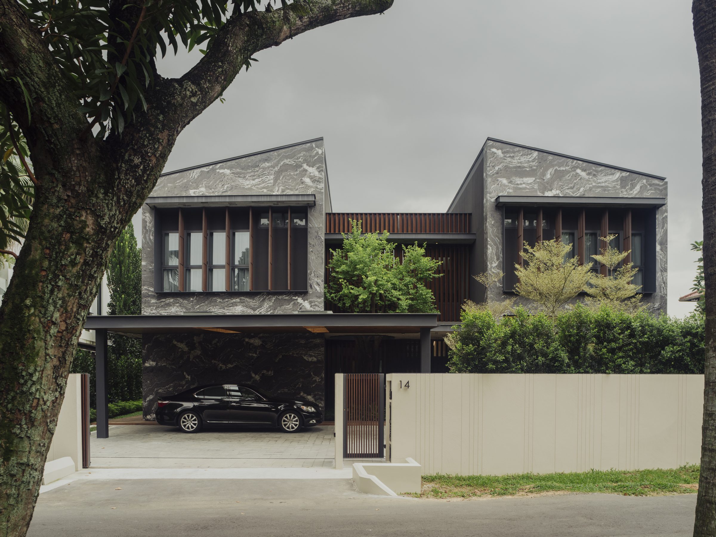 Front elevation in daylight, two marble-clad volumes joined by a planted central recess above the carport