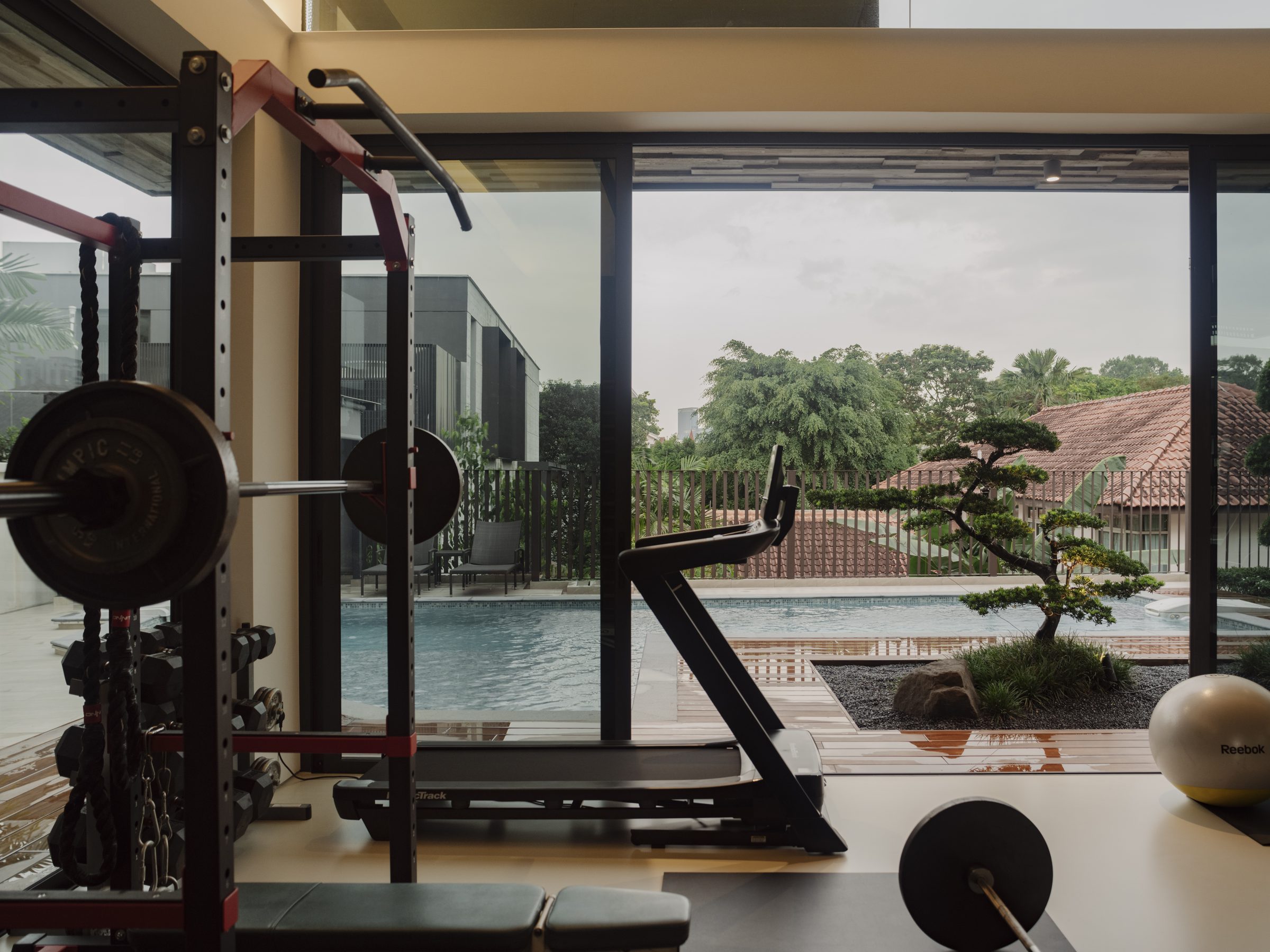 Home gym opening through full-height glazing to the pool and bonsai garden