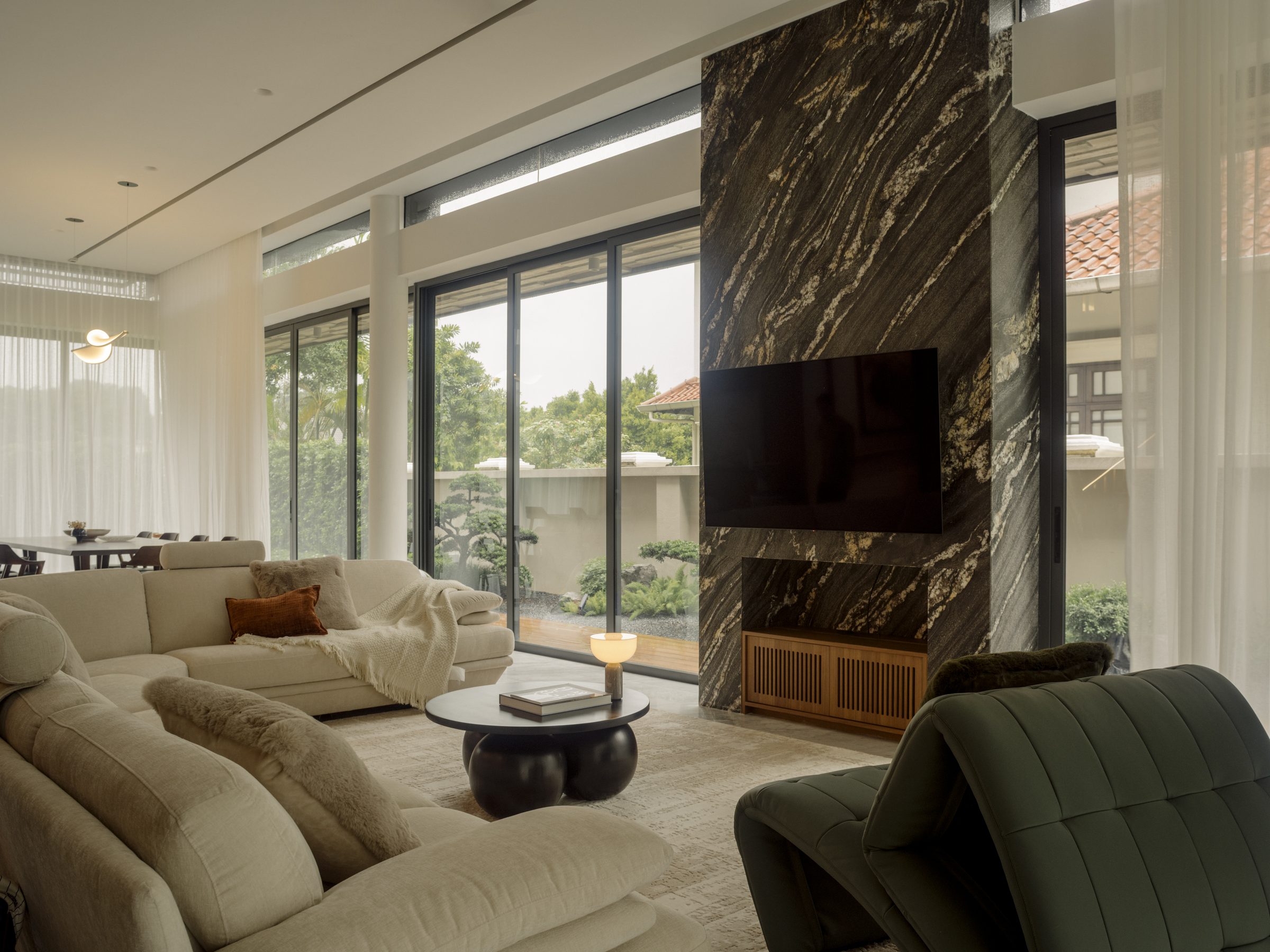 Living room with a figured dark marble feature wall, deep sofas and glazing to the garden on two sides