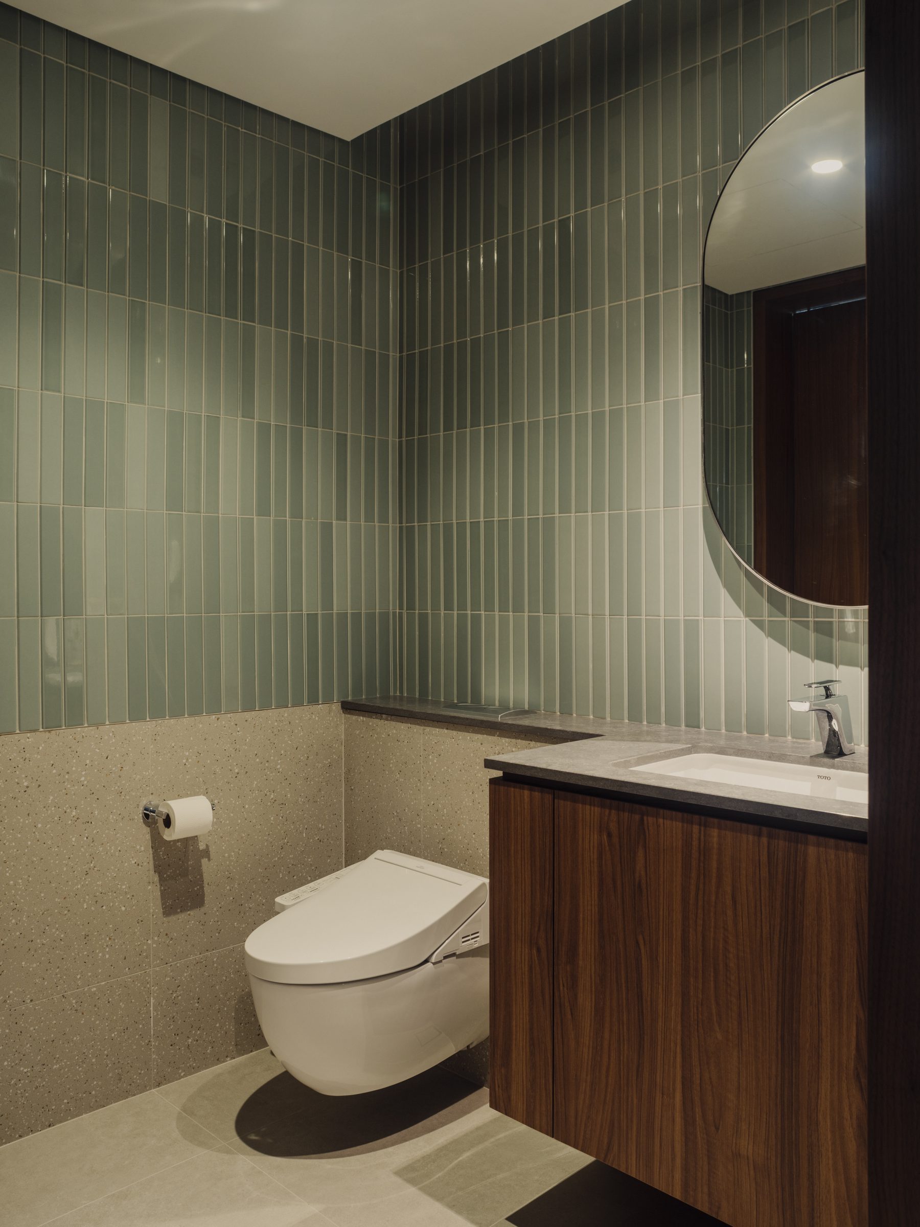 Powder room lined in green glazed tile, with an oval mirror above a timber vanity