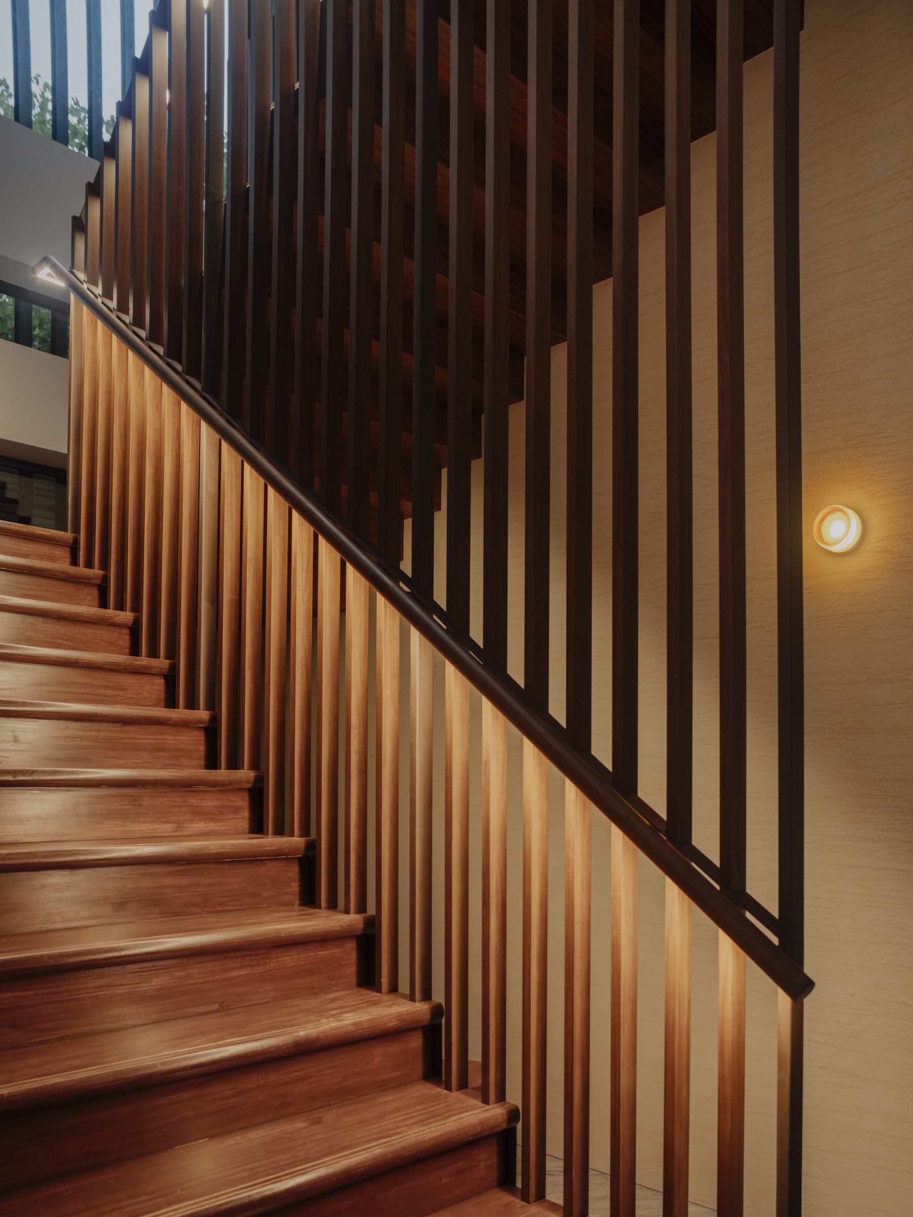 The stair rising in timber treads behind a fine vertical screen