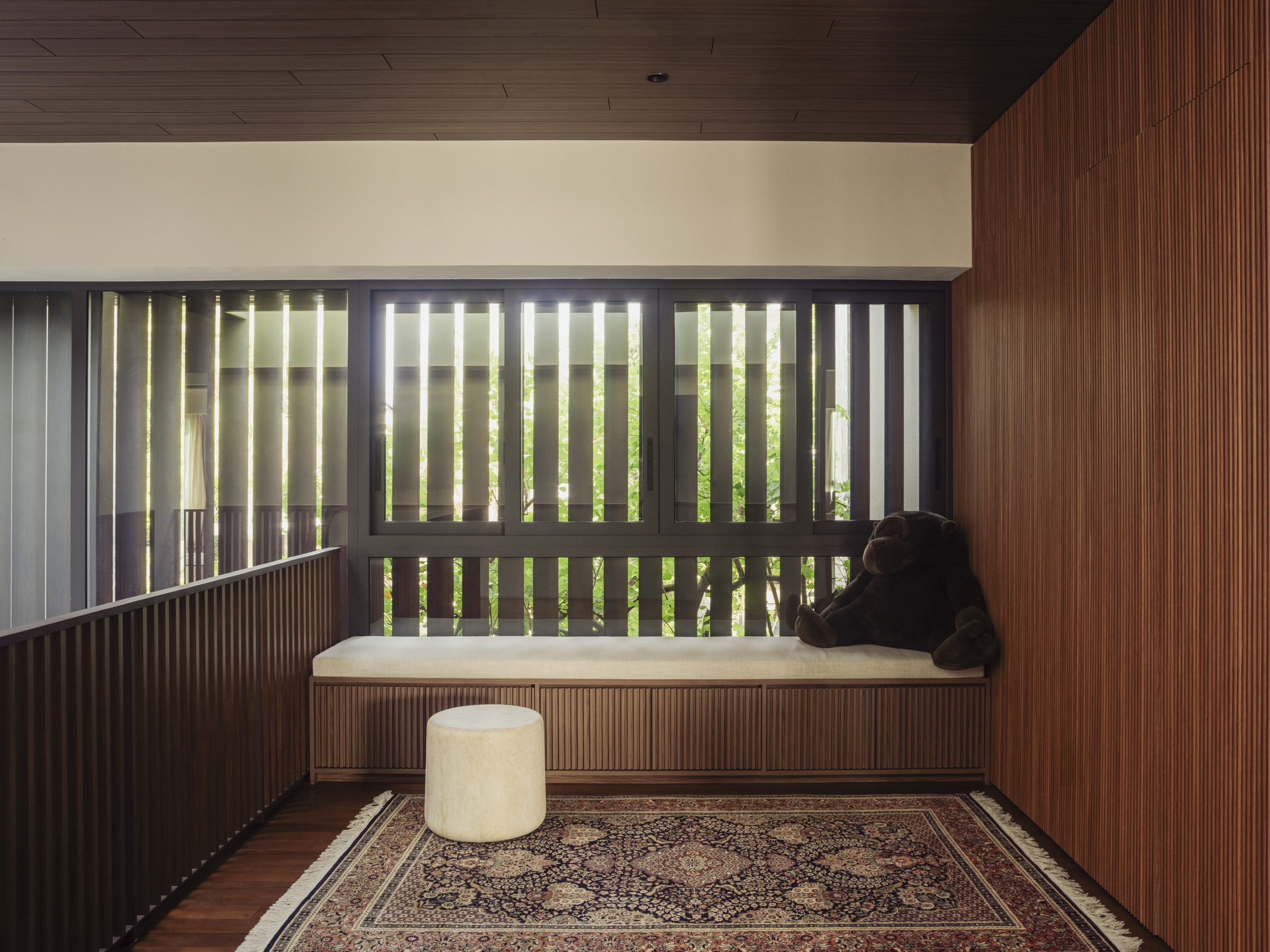 Window seat and rug in a timber-lined room, daylight filtered through vertical screens