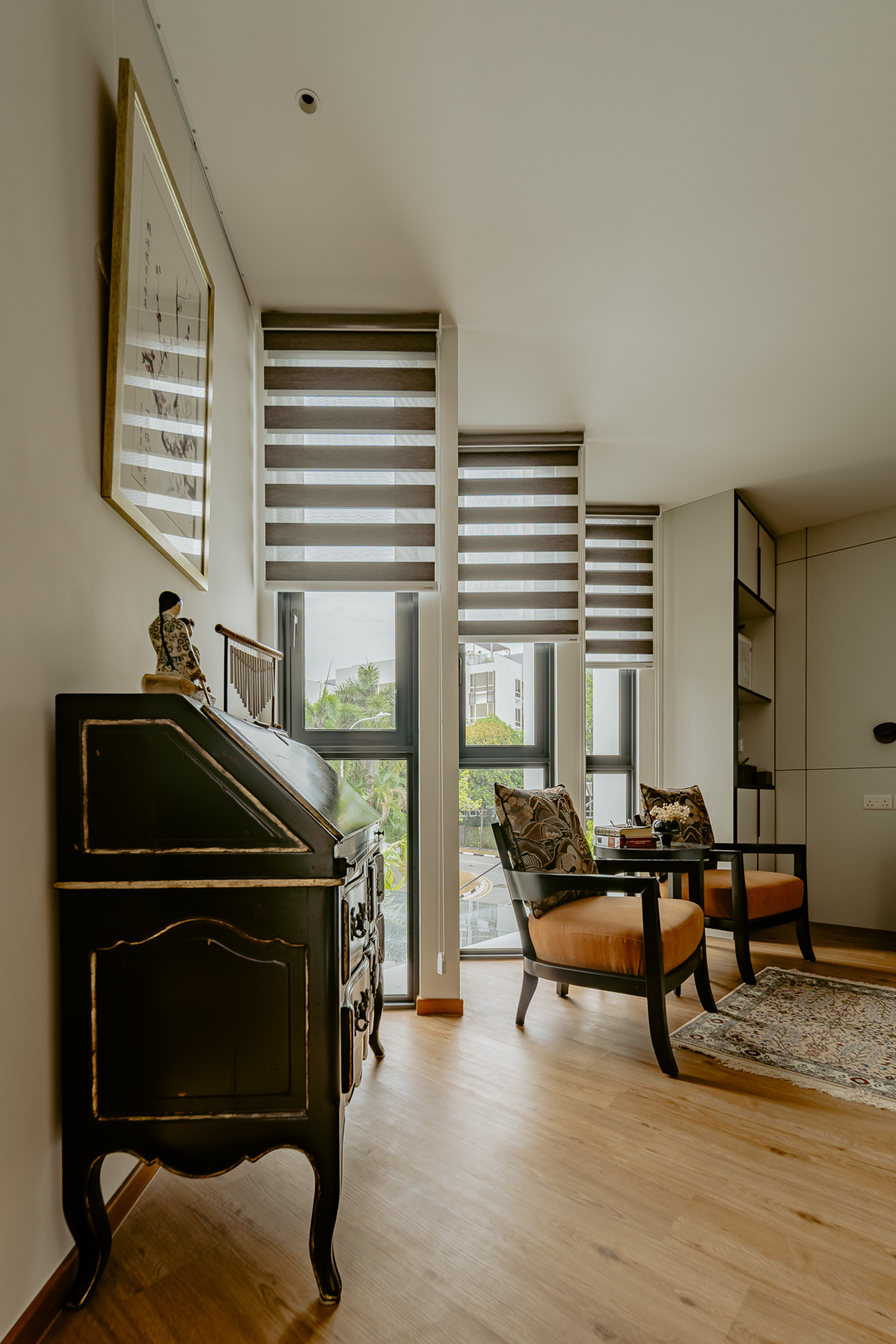 Sitting corner with an antique black bureau, a pair of armchairs and daylight through the angled windows