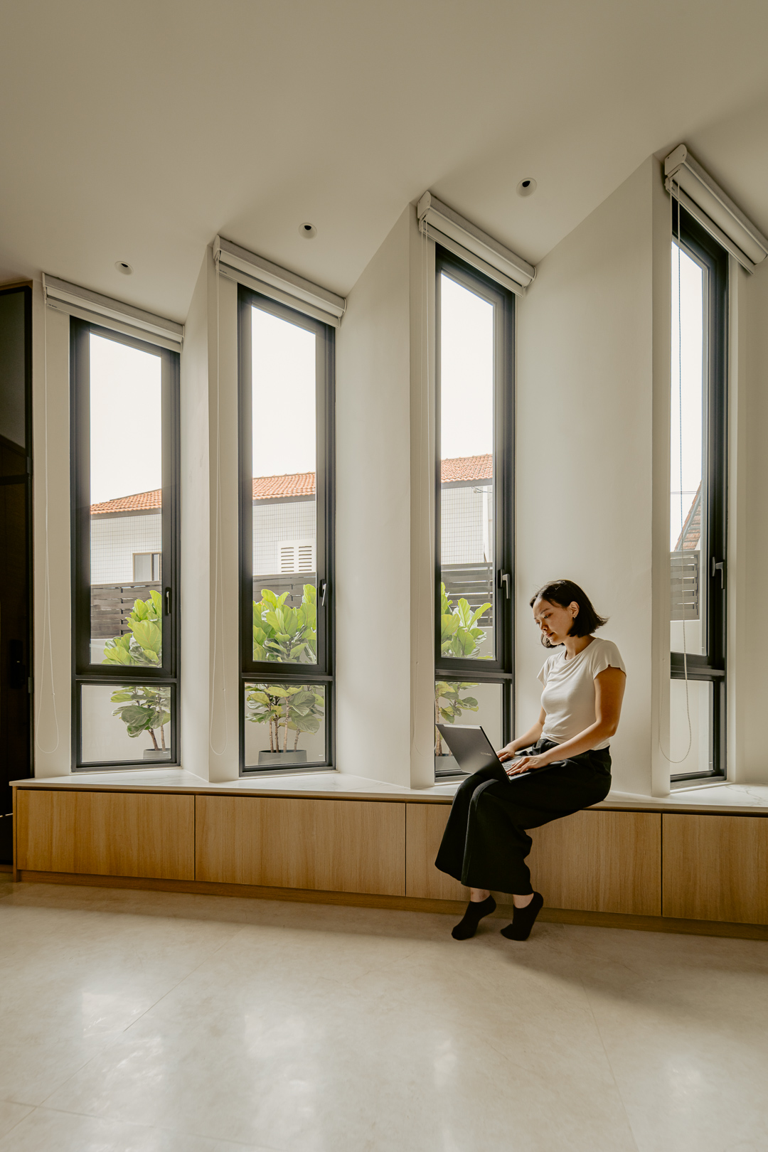 Timber window seat running beneath tall angled windows, with a resident working on a laptop