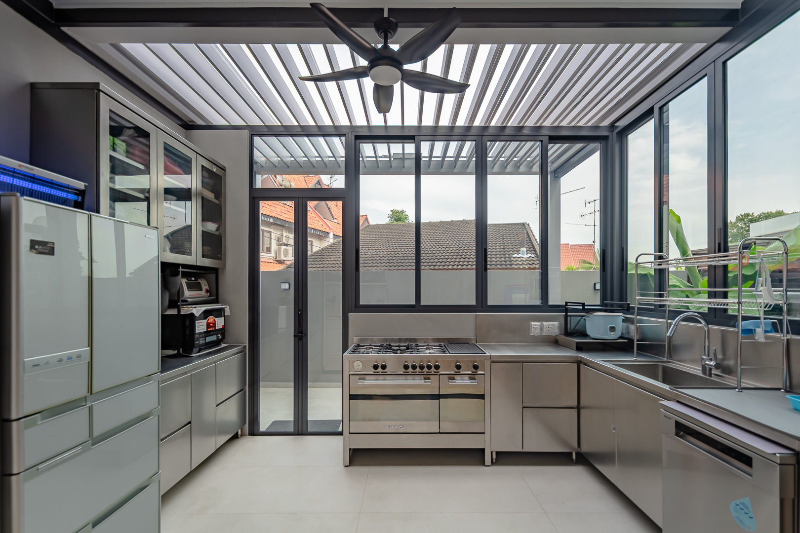 Wet kitchen under a louvred glass roof, with stainless steel counters and cabinetry along both walls