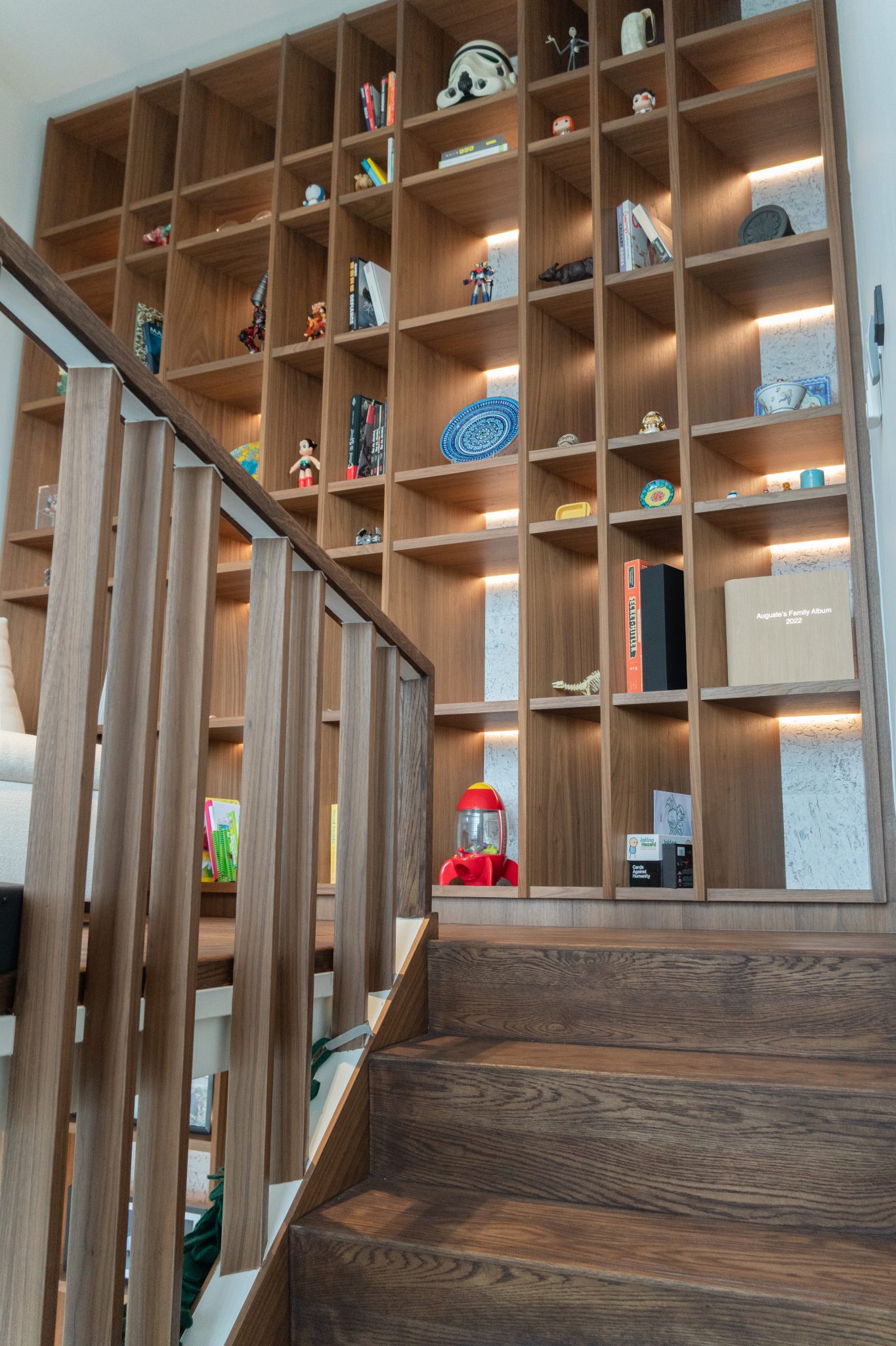 Tall walnut shelving display beside a timber staircase, holding books and a collection of small toys