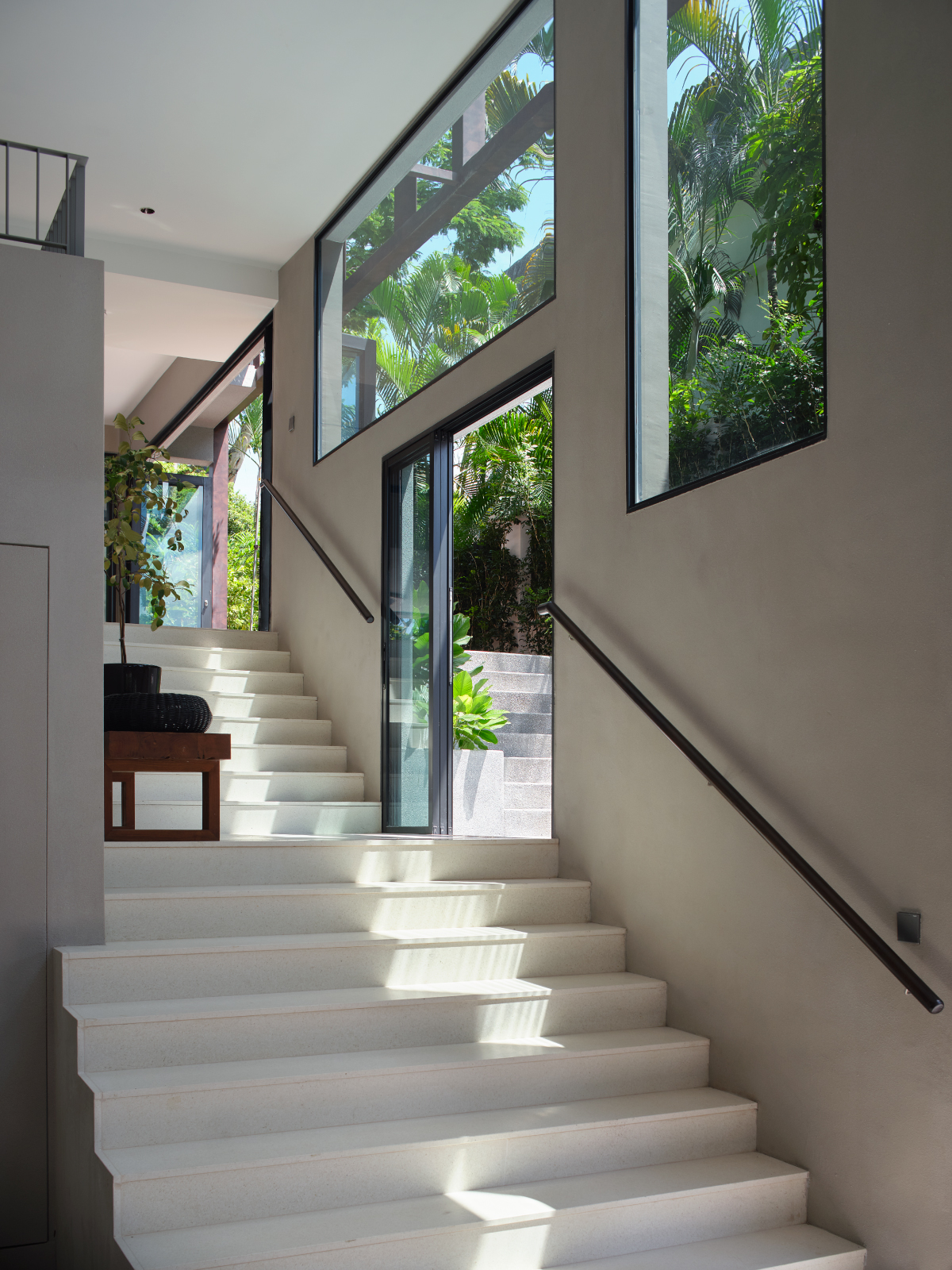 Pale stone staircase rising beside a full-height window that frames courtyard palms