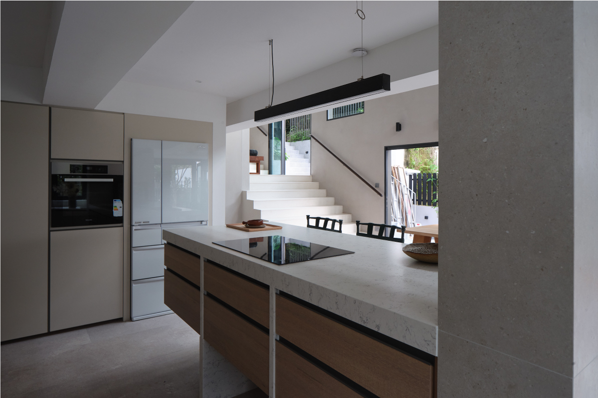 Open-plan kitchen with a stone-topped island, a concrete column and a stair rising to the garden beyond