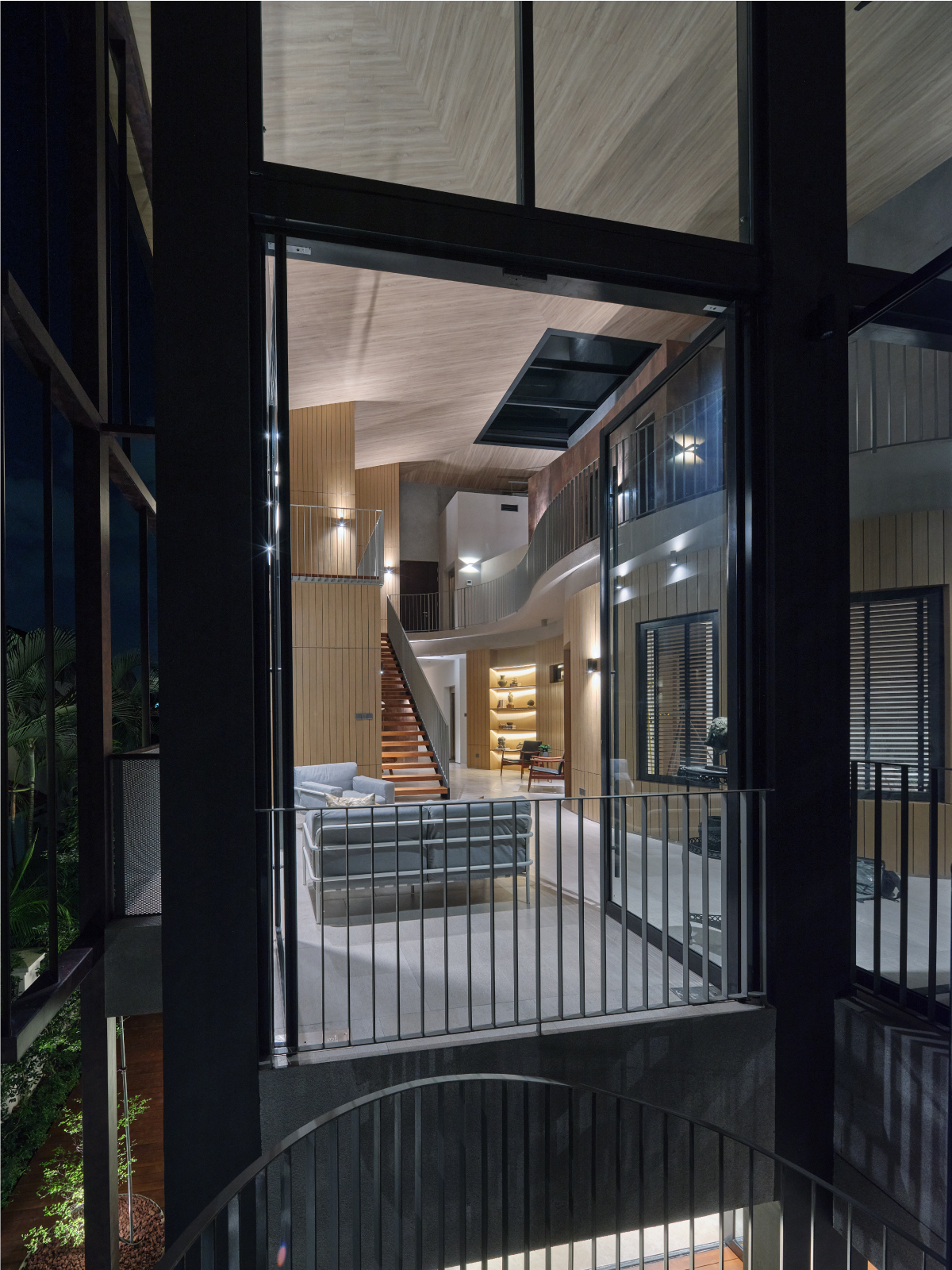 The double-volume living space at dusk, glimpsed through a glazed wall with the timber ceiling lit from within