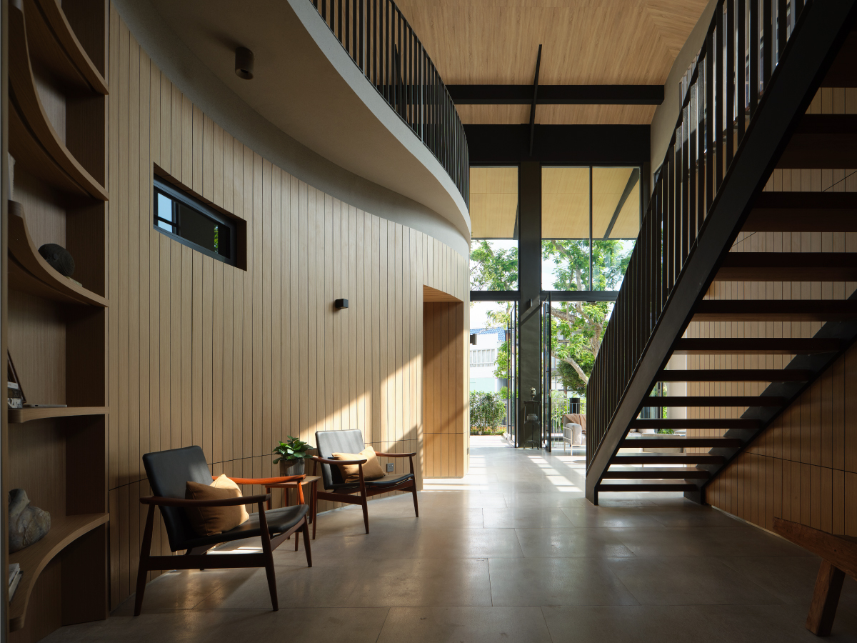 Double-height hall with a curved timber-clad wall, a black steel stair and a glazed wall onto the garden