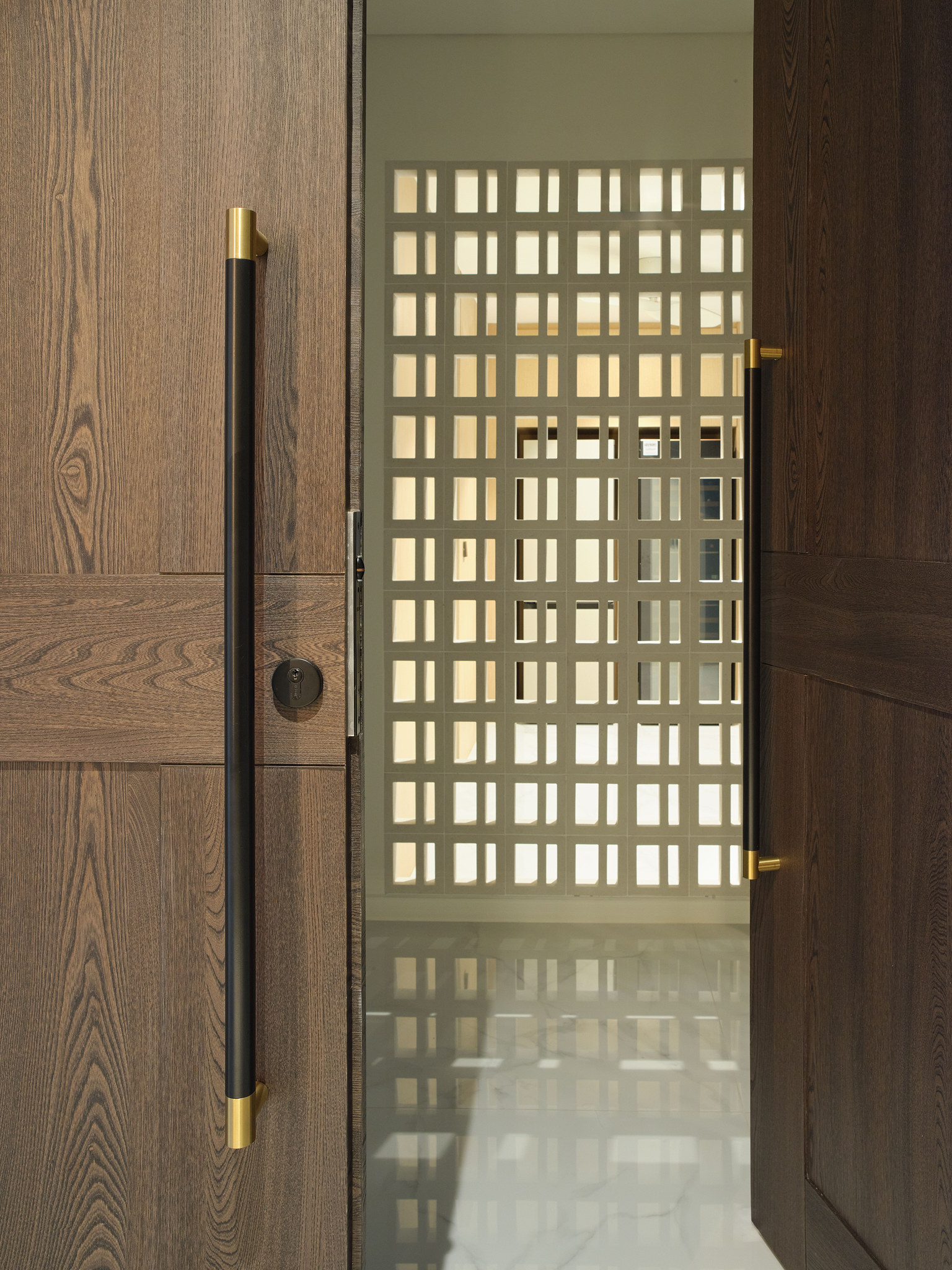 Timber entry door opening toward a perforated breeze-block screen catching daylight