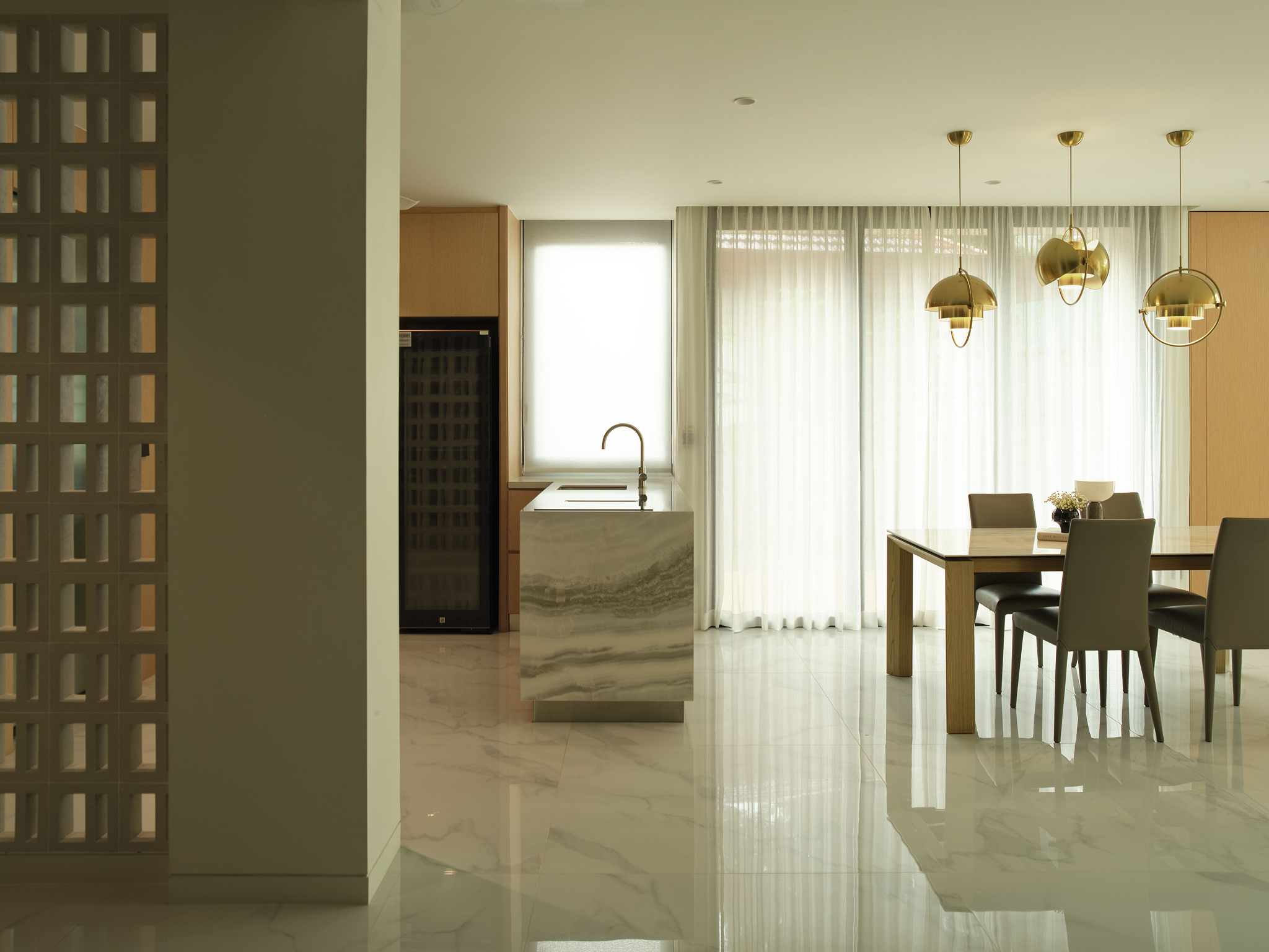 Kitchen with a marble-clad island and brass pendant lights over a timber dining table