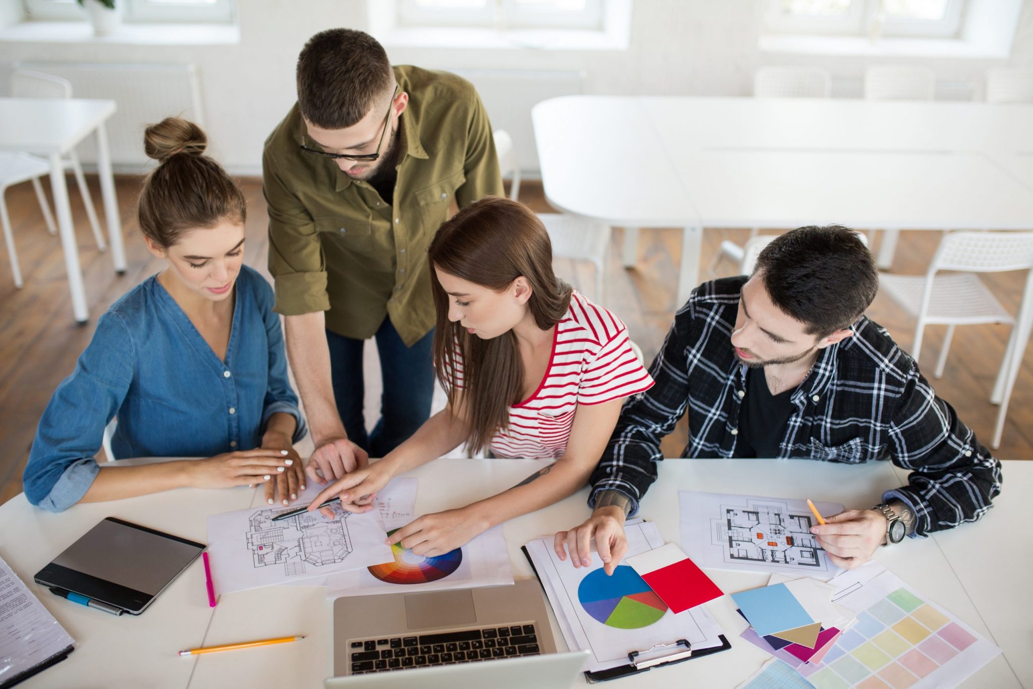 Group of business men and women working with sketches and laptop spending time at work. Young creative people thoughtfully discussing work together in modern office